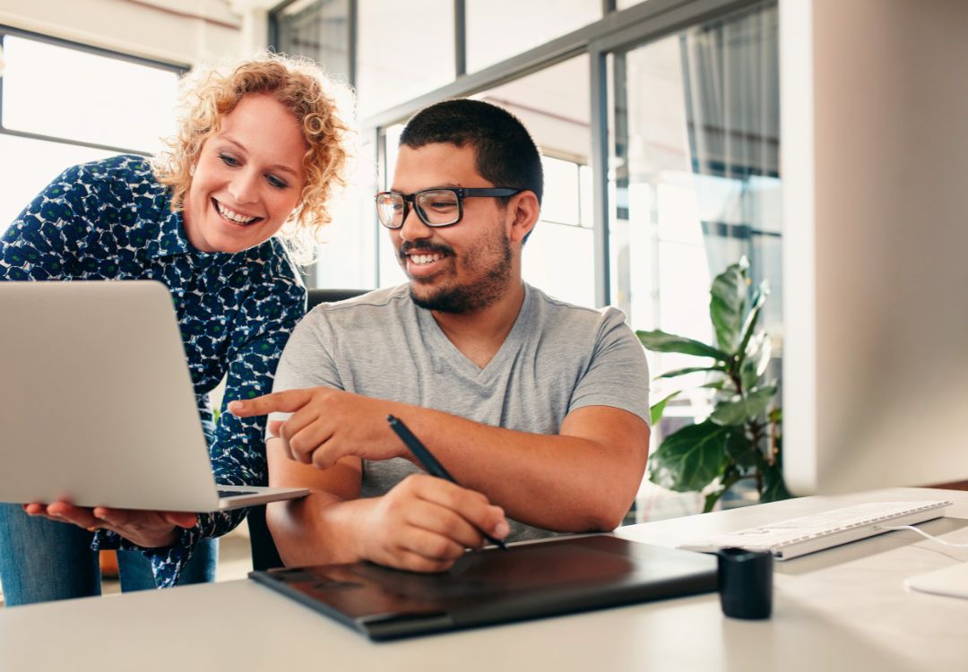 Two students collaborating on master herbalist certificate coursework with laptop and tablet in bright office