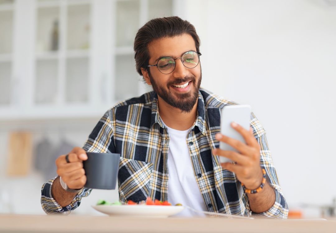 Smiling male doctorate student with healthy meal and coffee at home representing KCNH lifestyle integration