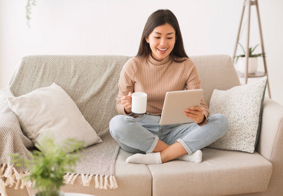 Female doctoral student studying biblical studies on tablet at home with coffee on couch
